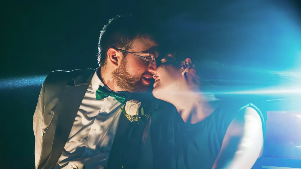 couple kissing in front of car headlights at night