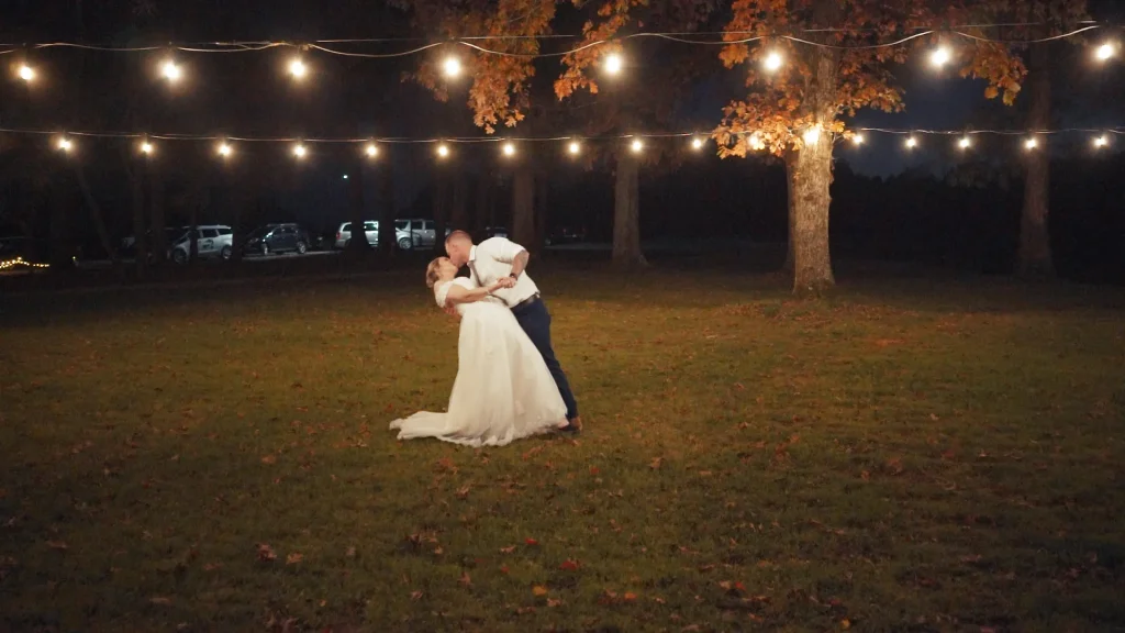 Groom dipping bride and kissing under string lights at, Barn at Gully Tavern